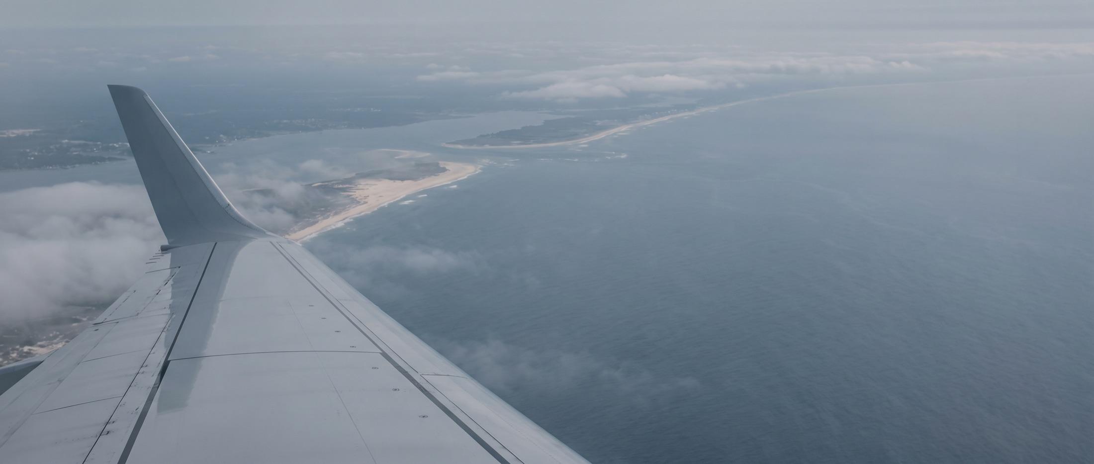 Aircraft wing above a muted coastline seen from the cabin window